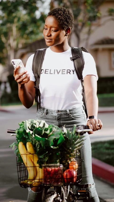 a woman standing next to a bicycle holding a cell phone, trending on pexels, renaissance, logo for lunch delivery, wearing a t-shirt, salad, dark-skinned