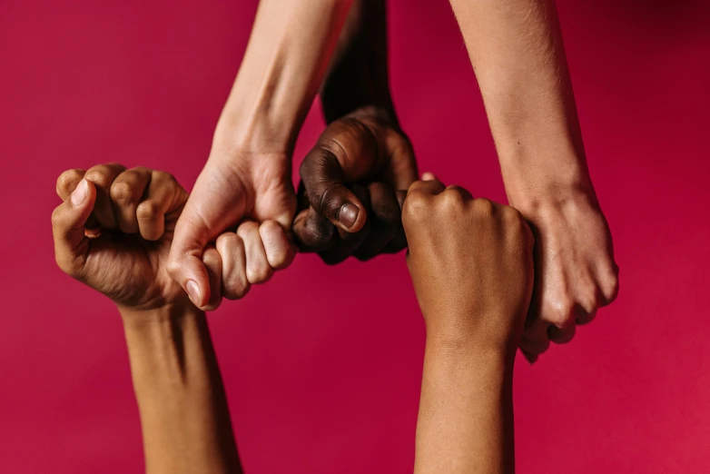 a group of people holding their hands together, by Arabella Rankin, trending on pexels, in red background, holding a staff, with brown skin, strength