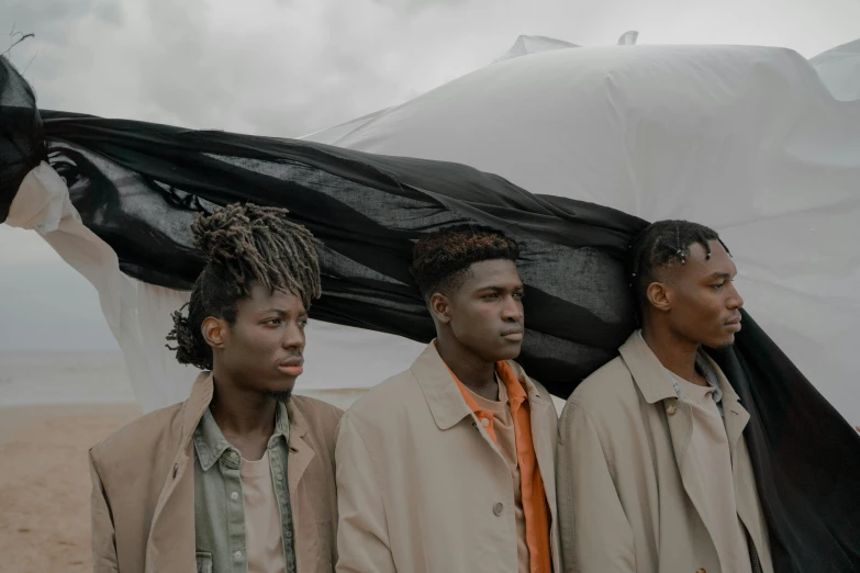 a group of men standing next to each other on a beach, an album cover, by Matija Jama, pexels contest winner, afrofuturism, wearing a trenchcoat, on a cloudy day, black teenage boy, refugees