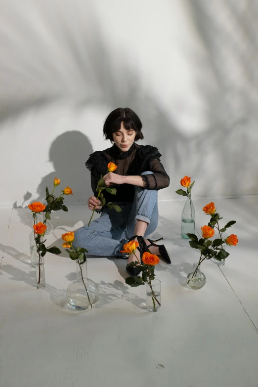 a woman sitting on the ground surrounded by flowers, an album cover, by Winona Nelson, alice cullen, in a white room, high quality photo, in front of an orange background