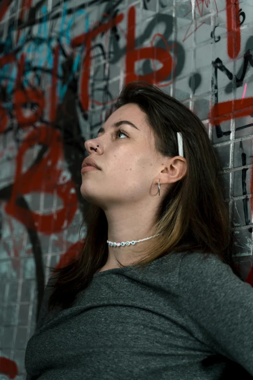 a woman leaning against a wall with graffiti on it, an album cover, inspired by Elsa Bleda, trending on pexels, graffiti, steel choker, headshot profile picture, charli bowater, hyperrealism photo