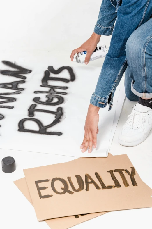 a woman kneeling in front of a sign that says equality, by Arabella Rankin, trending on unsplash, blotch of spray paint in corner, on a white table, jeans and t shirt, formulas