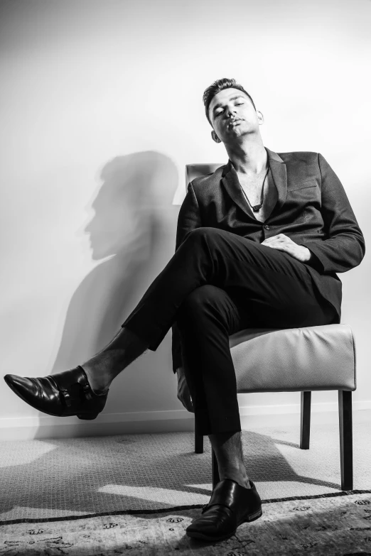 a black and white photo of a man sitting on a chair, style of kilian eng, focus on his foot, marton csokas, brightly lit