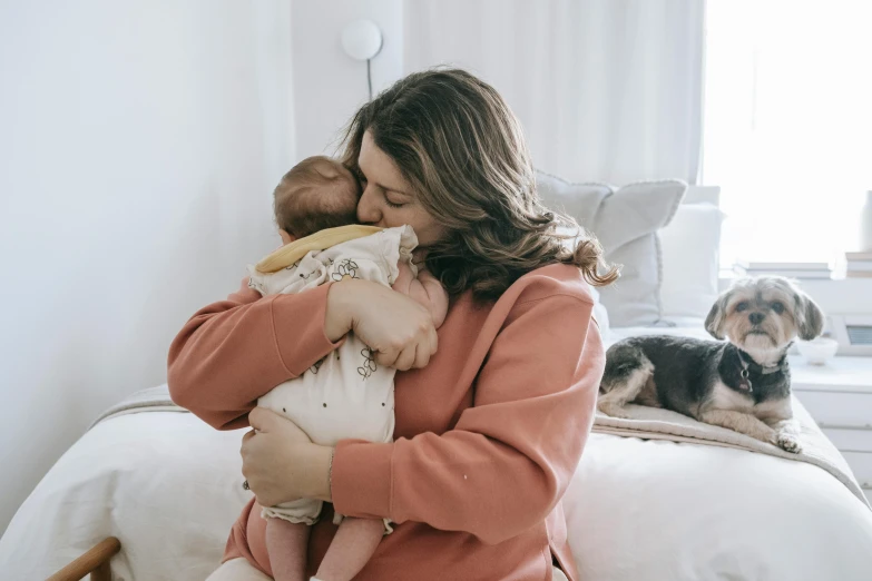a woman sitting on top of a bed holding a baby, pexels contest winner, hugging each other, australian, wearing a pink hoodie, 1 4 9 3