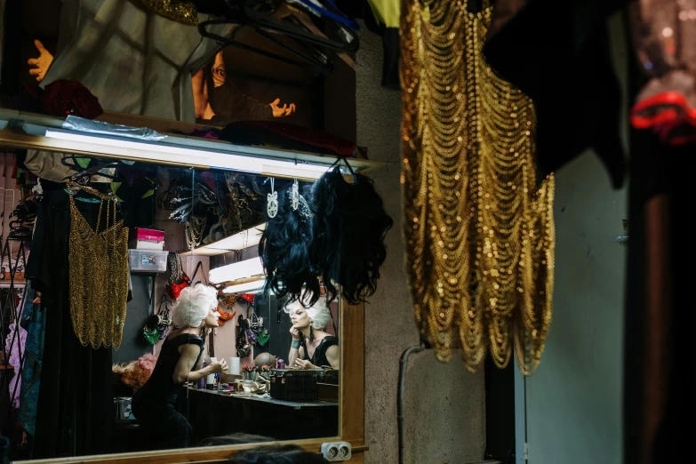 a man that is standing in front of a mirror, by Elsa Bleda, pexels contest winner, baroque, theater dressing room, feather boa, inside a shed, in dark robes with gold accents