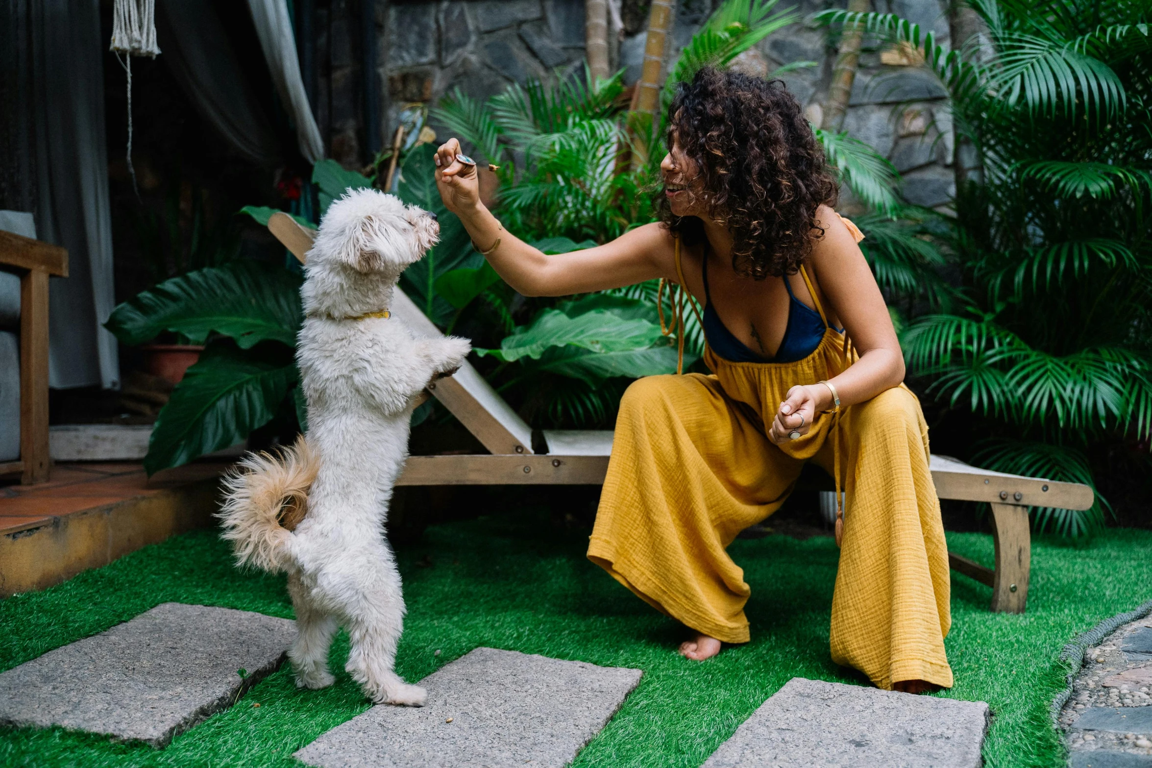 a woman sitting on a bench petting a dog, pexels contest winner, bali, waving, in garden, nathalie emmanuel