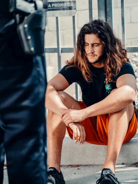 a man sitting on the ground next to a police officer, a colorized photo, trending on pexels, long brown wavy hair, bra and shorts streetwear, in jail, portrait featured on unsplash