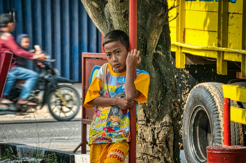 a young boy standing next to a tree in front of a truck, pexels contest winner, south jakarta, avatar image, yellow clothes, square