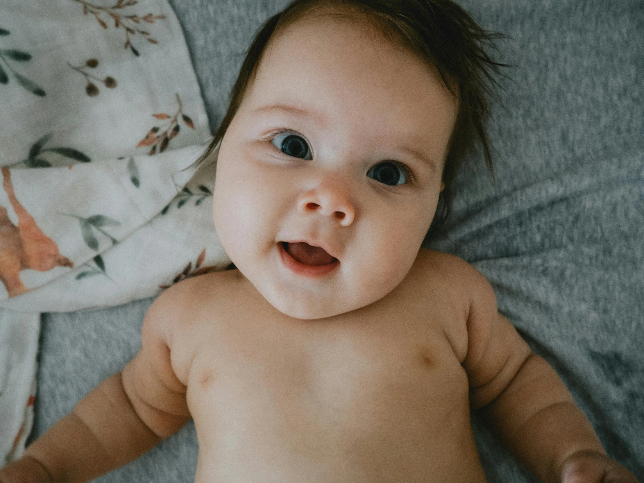 a baby laying on top of a bed next to a blanket, pexels contest winner, looking up at camera, closeup portrait shot, gif, grinning lasciviously