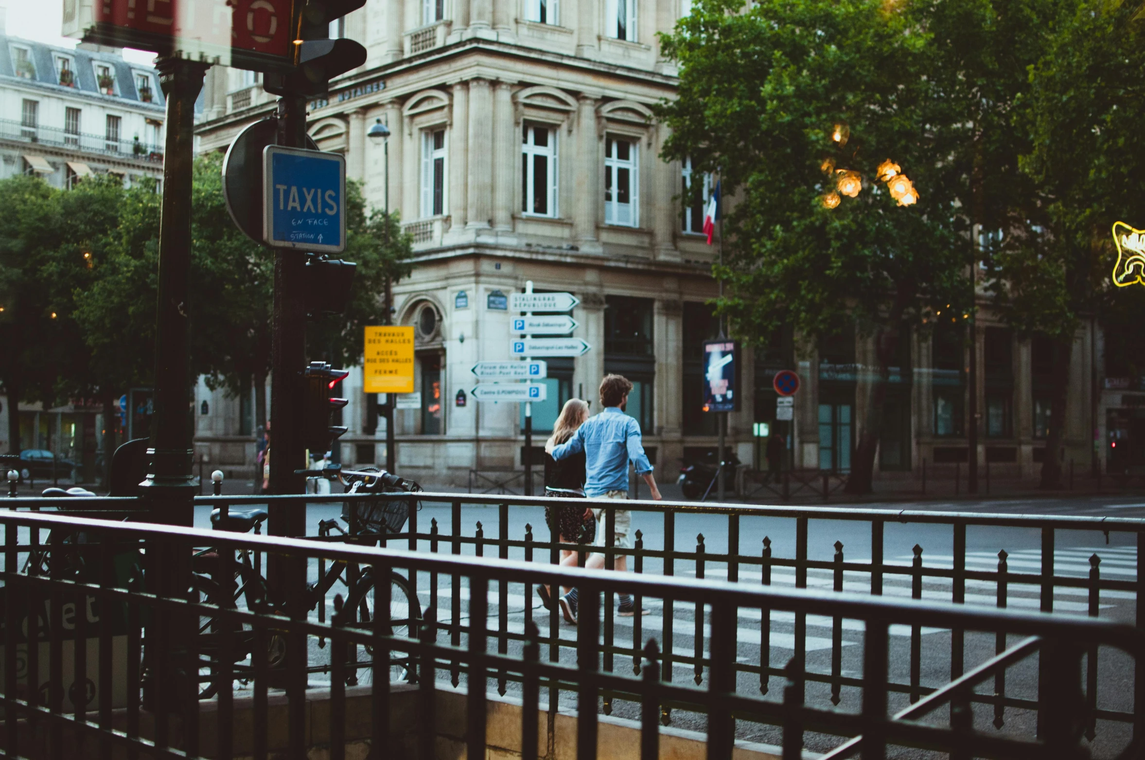 a man walking across a street next to a tall building, pexels contest winner, paris school, barriers, summer evening, with his back turned, lush surroundings