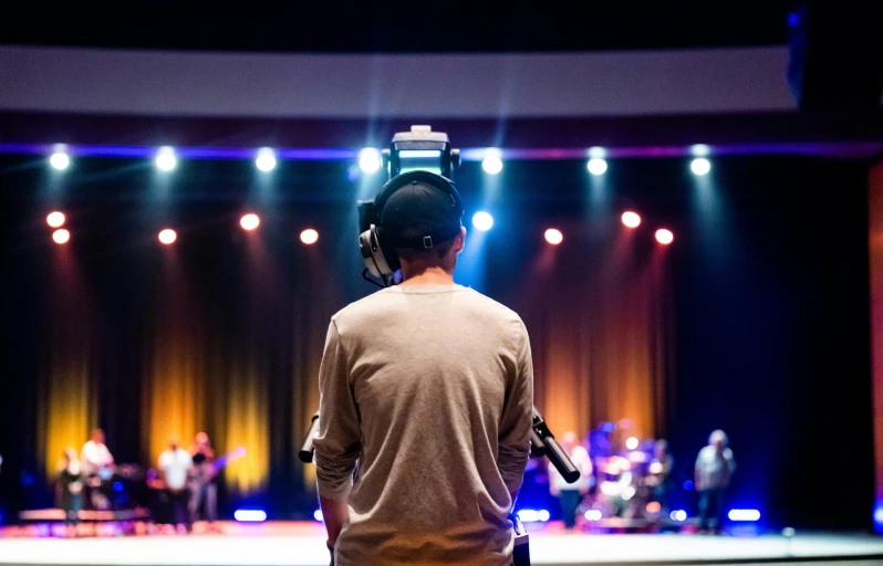 a man standing in front of a stage with a microphone, by Dan Content, pexels, happening, church background, back facing the camera, tv production, high school