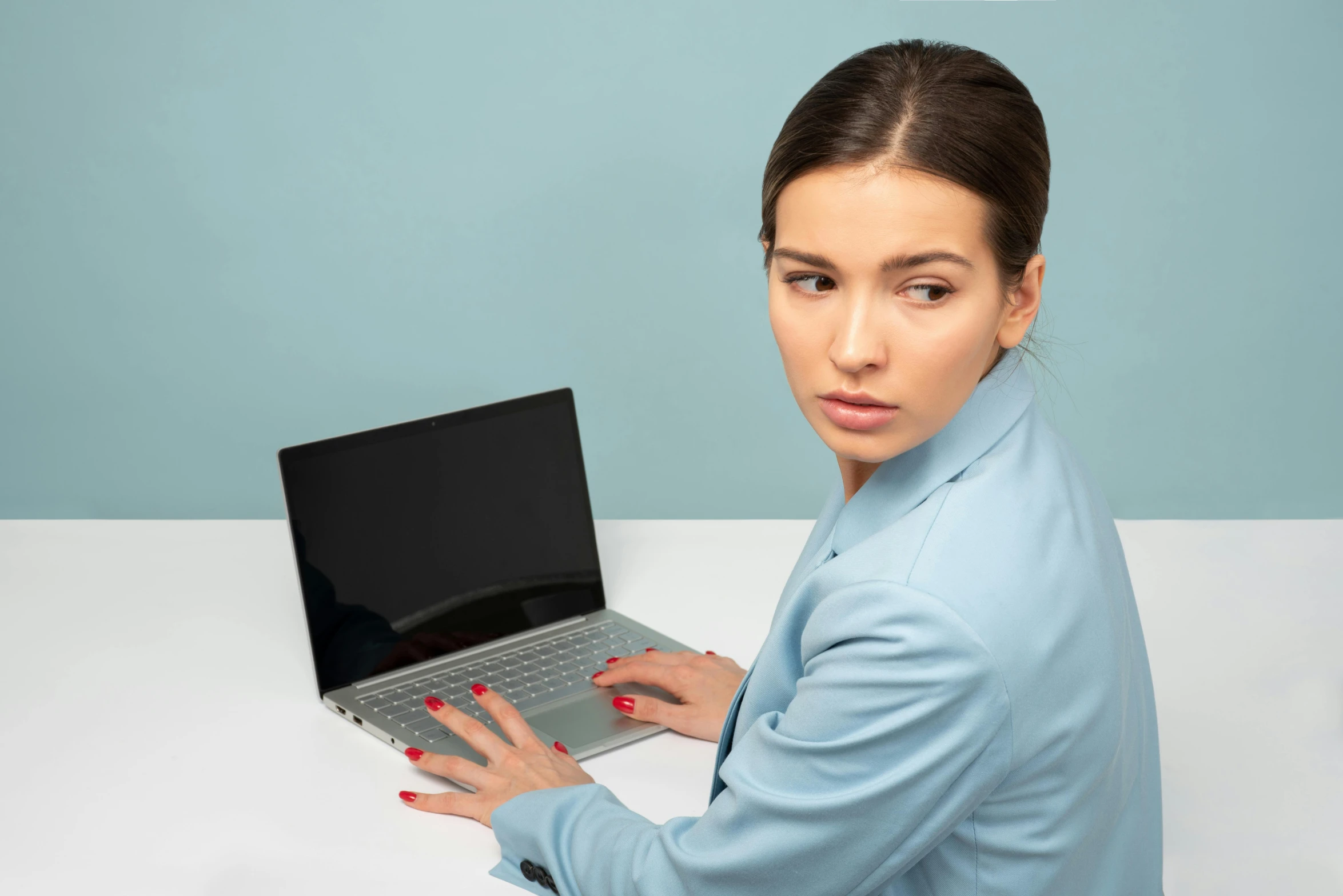 a woman sitting at a table with a laptop, light blue skin, modelling, frowning, no text