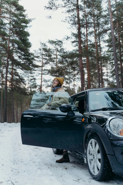 a person standing next to a car in the snow, in the middle of a forest, mini cooper, profile image, festivals