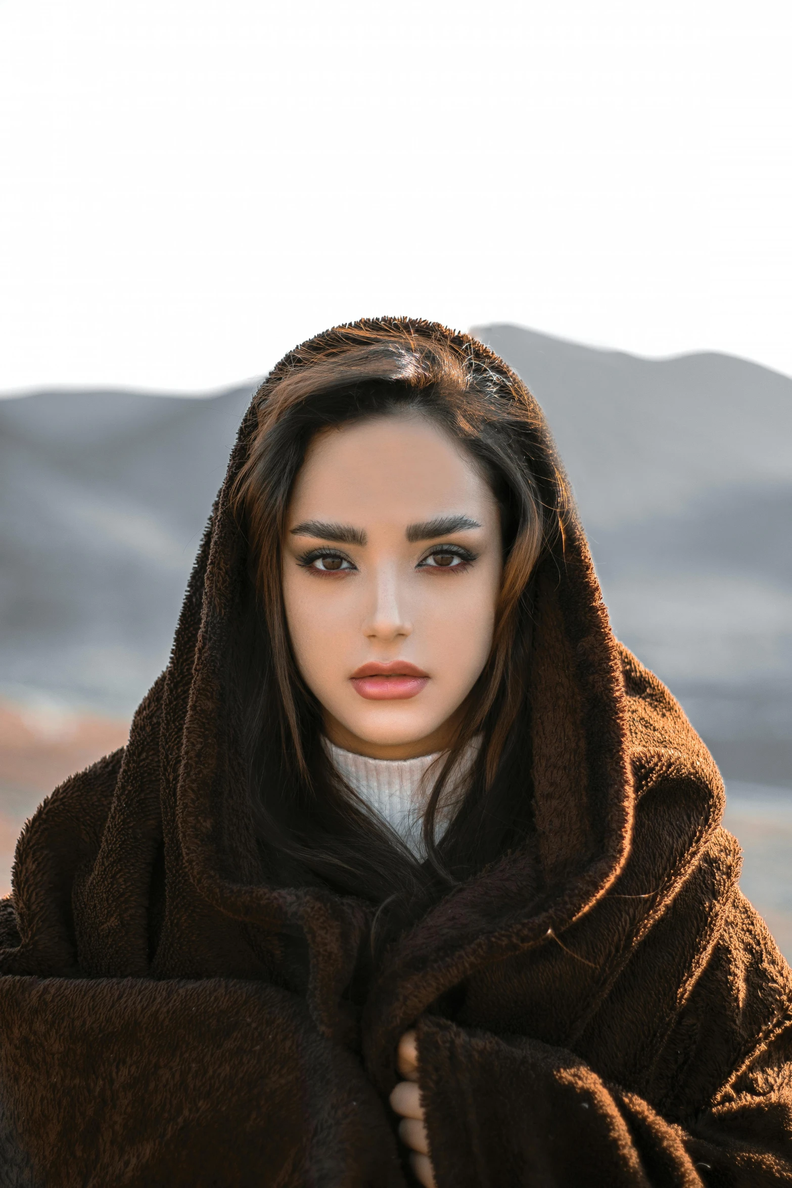 a woman wrapped in a blanket in the desert, an album cover, by irakli nadar, trending on pexels, asian beautiful face, brown sweater, persian princess, wearing hoodie
