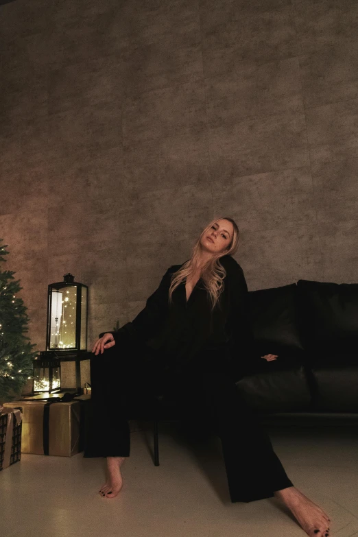 a woman sitting on a couch next to a christmas tree, reddit, minimalism, wearing black silk robes, long ashy hair | gentle lighting, blonde, profile image