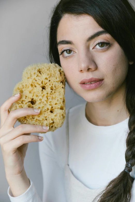 a woman holding a sponge up to her face, detailed product image, looking to the side off camera, organic and intricate, crispy quality