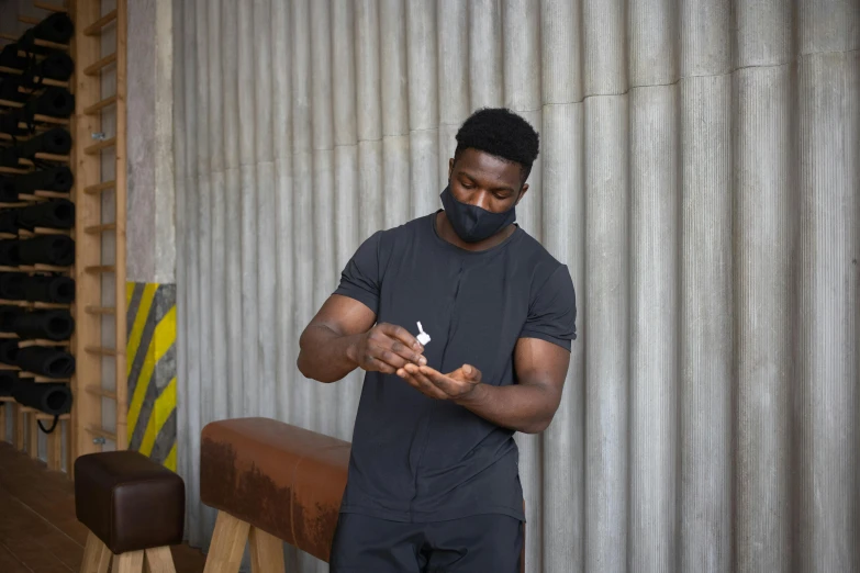 a man standing next to a bench holding a cell phone, face mask, body building blacksmith, profile image, black man