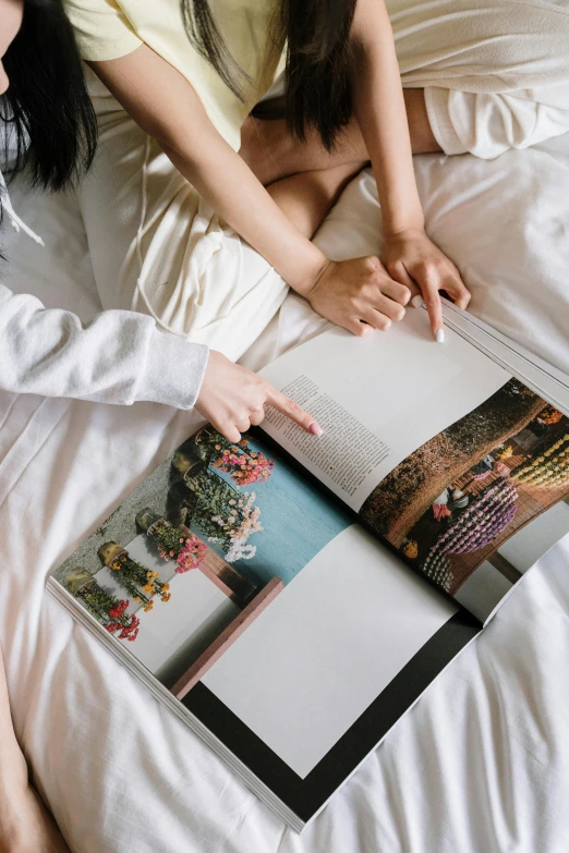 a couple of women sitting on top of a bed, a picture, unsplash contest winner, visual art, print on magazine, children's book, high angle close up shot, slightly pixelated