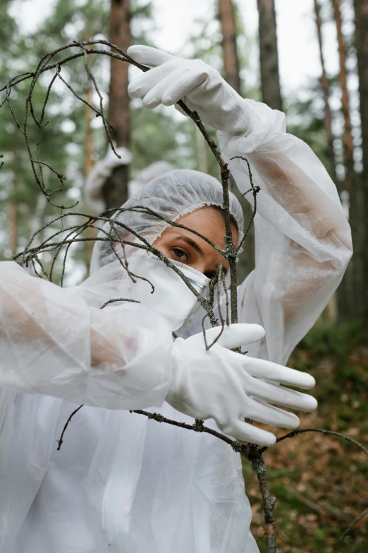 a woman in a white coverall in the woods, inspired by Marina Abramović, pexels contest winner, environmental art, flight suit and gloves, funeral veil, branches, healthcare worker