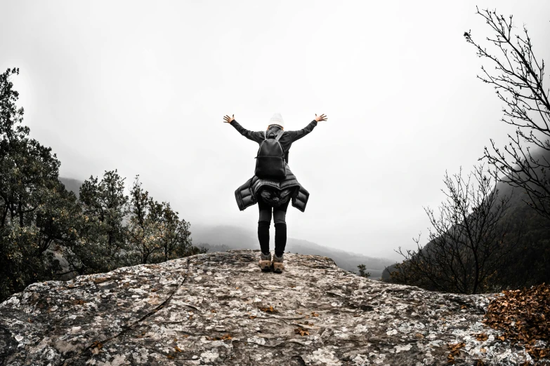 a person standing on top of a large rock, pexels contest winner, happening, pose(arms up + happy), grey, with a backpack, slight overcast