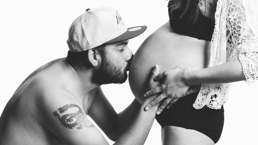 a black and white photo of a man kissing a pregnant woman, by Lucia Peka, belly button showing, andrew gonzalez, ffffound, tattoo