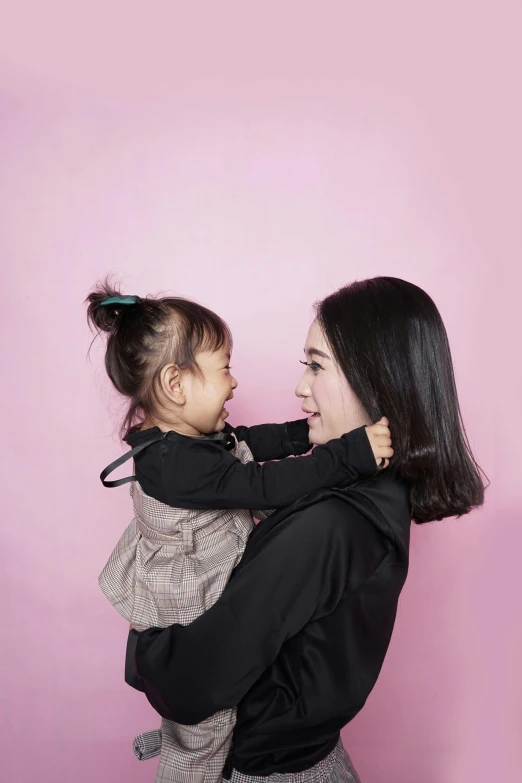 a woman holding a baby in her arms, inspired by Cui Bai, pexels contest winner, minimalism, pink background, ponytail black hair, jakarta, lesbian