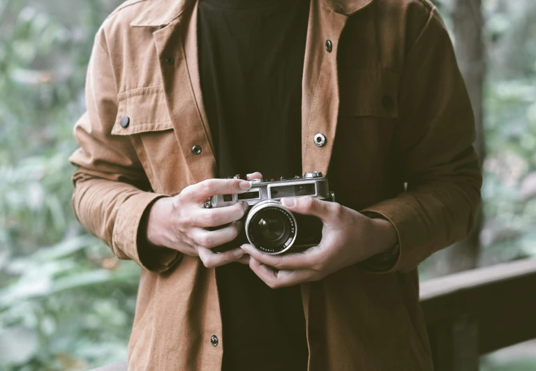 a man holding a camera in his hands, trending on unsplash, brown jacket, vintage aesthetic, fan favorite, medium format