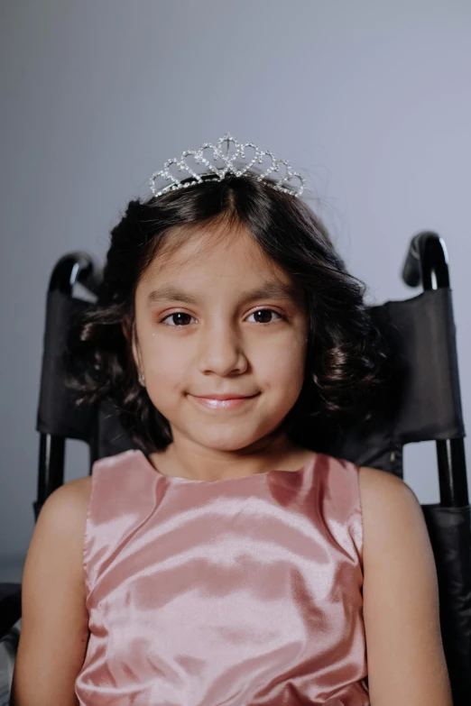 a little girl wearing a tiara sitting in a chair, an album cover, shutterstock contest winner, wheelchair, modeling for dulce and gabanna, close-up portrait film still, proud looking