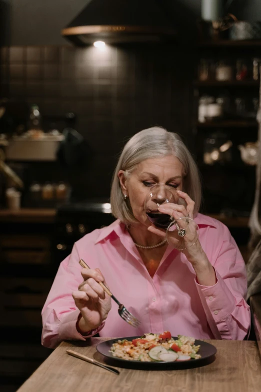 a woman sitting at a table with a plate of food, drinking wine, holding a kitchen knife, shot with sony alpha, white haired lady