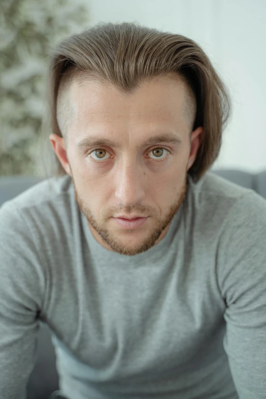 a man sitting on a couch with a remote in his hand, a character portrait, trending on reddit, hyperrealism, large eyes with visible pupils, mullet long haircut, ultra realistic 8k octan photo, acting headshot