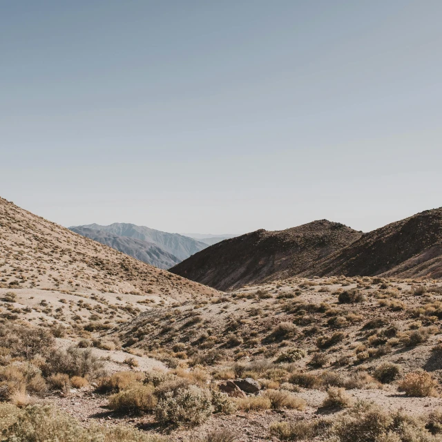 a man riding a motorcycle down a dirt road, by Ryan Pancoast, trending on unsplash, visual art, death valley, sparse vegetation, on top of a mountain, campsites