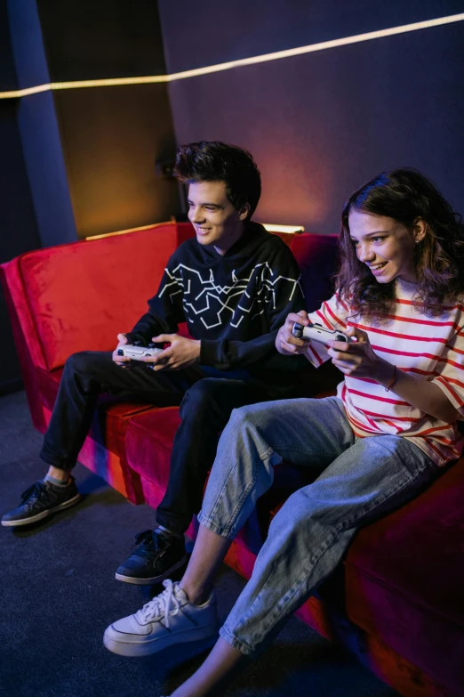 a couple of people sitting on top of a red couch, by John Luke, holding controller, teenagers, promotional image, playing games