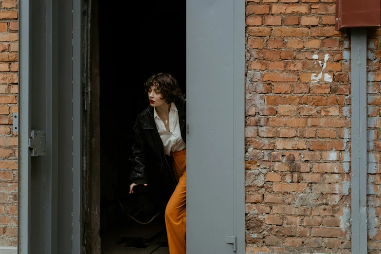 a woman standing in the doorway of a brick building, inspired by Elsa Bleda, pexels contest winner, bauhaus, detective clothes, finn wolfhard, фото девушка курит, leather clothing