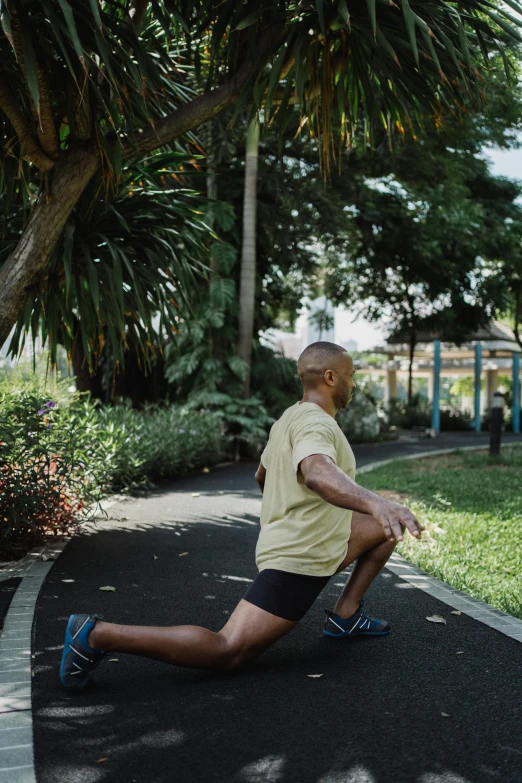 a man riding a skateboard down a sidewalk, stretching her legs on the grass, with palm trees in the back, local gym, standing in a botanical garden