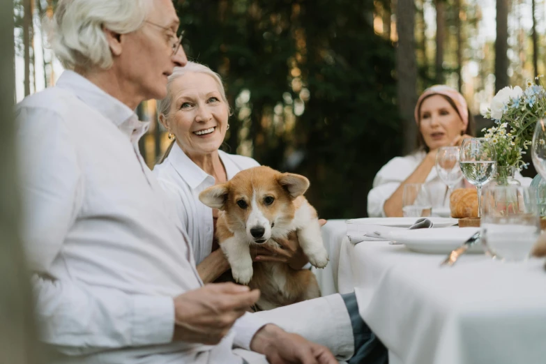 a group of people sitting around a table with a dog, white - haired fox, wearing a white button up shirt, al fresco, with accurate features