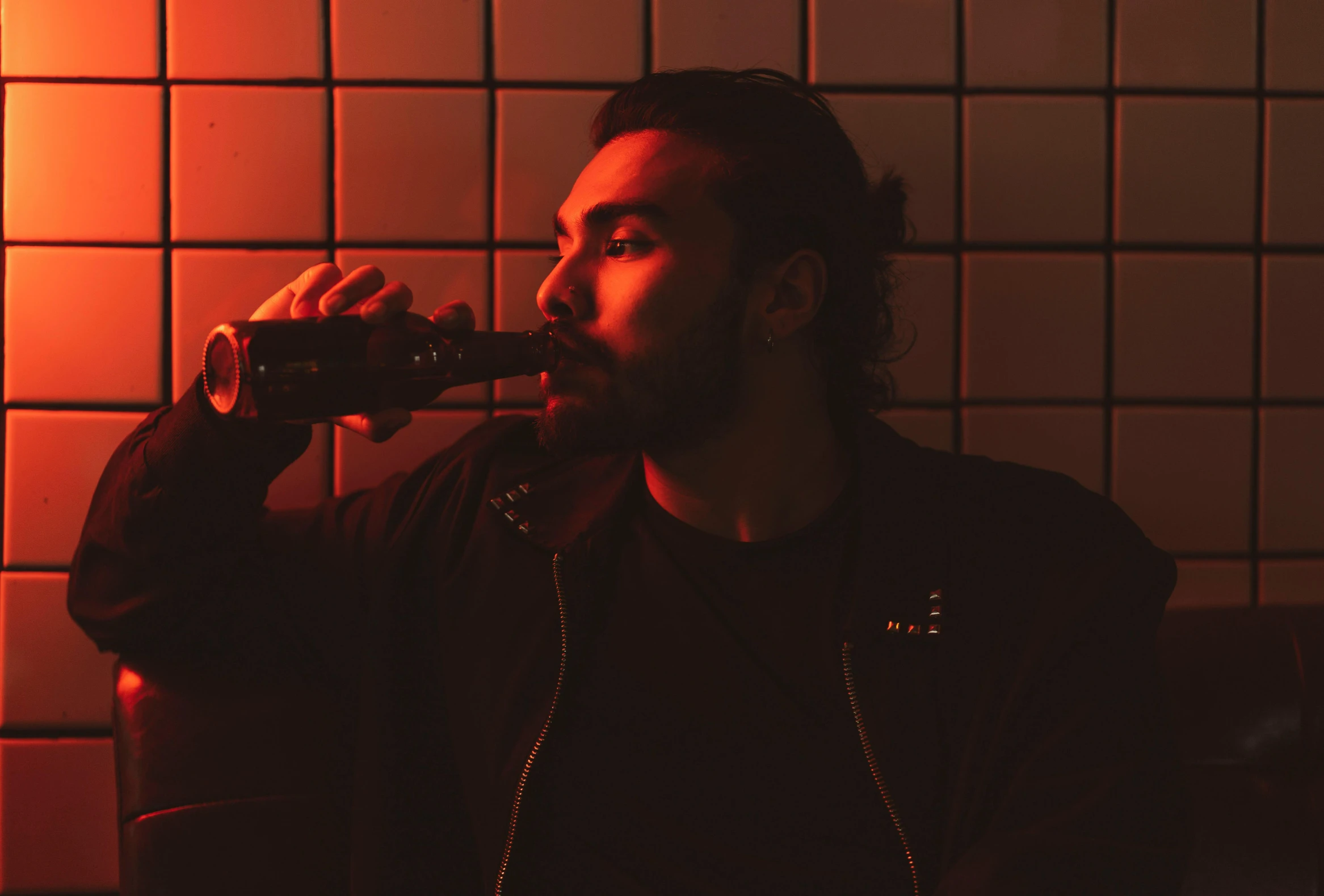 a man drinking from a bottle in a dimly lit room, an album cover, pexels contest winner, charli xcx, with a beard and a black shirt, redscale photography, bright lights