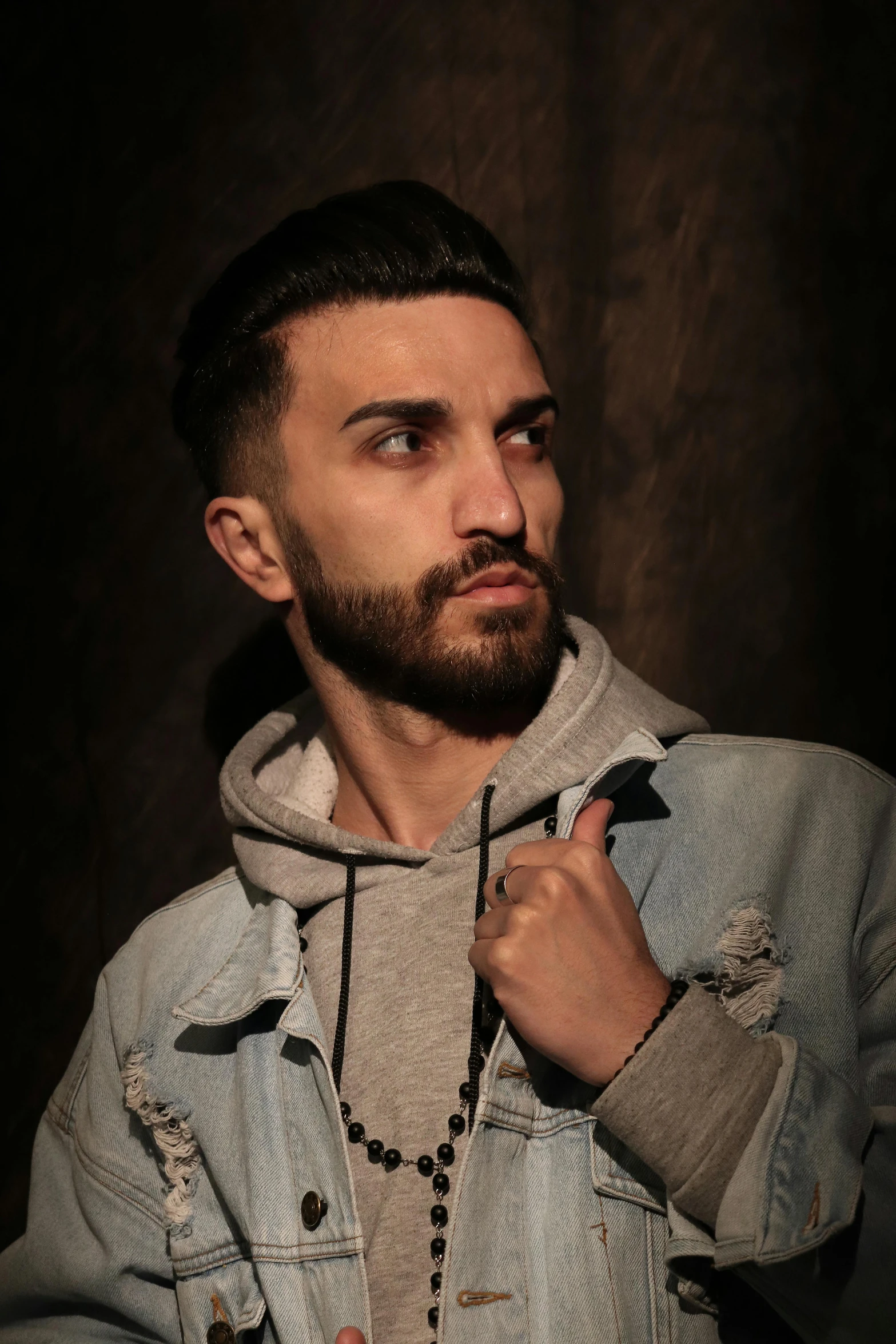 a man with a beard wearing a denim jacket, an album cover, inspired by Adam Szentpétery, mannerism, he is wearing a brown sweater, sayem reza, looking to the side off camera, androgynous male