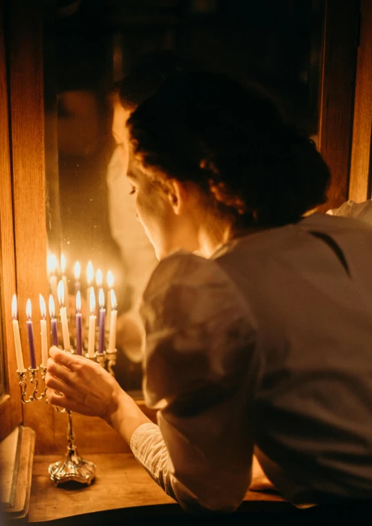 a man and a woman lighting candles on a menorah, by Emanuel Witz, pexels, renaissance, looking into a mirror, half image, warm lighting inside, beautiful jewish woman