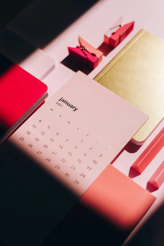 a calendar sitting on top of a desk next to a keyboard, by Julia Pishtar, trending on unsplash, pink and red color scheme, lit from above, synthetic materials, elegantly dressed