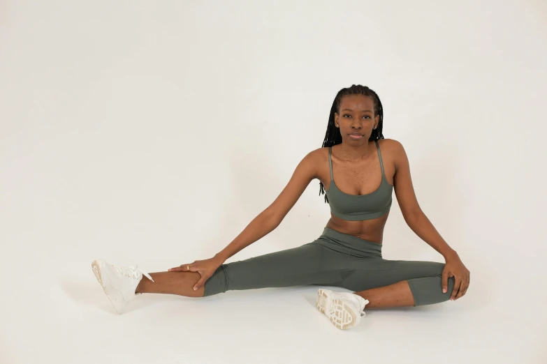 a woman in a sports bra top and leggings sitting on the floor, trending on pexels, arabesque, muted green, adut akech, lunging at camera :4, satisfied pose