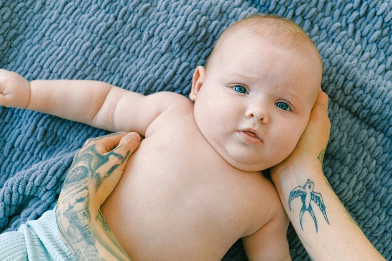 a close up of a person holding a baby, a tattoo, pexels contest winner, lying down, piercing blue eyes, arms crossed on chest, full body image