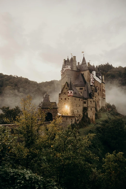 a castle sitting on top of a lush green hillside, unsplash contest winner, german romanticism, gloomy misty atmosphere, brown, twilight, neo - gothic architecture