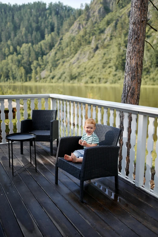 a baby sitting in a chair on a deck, by Jaakko Mattila, unsplash, square, in a scenic environment, black armchair, drinking