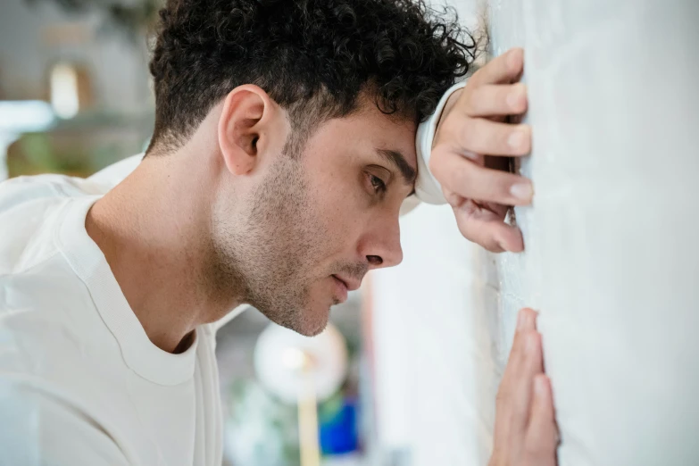 a man leaning against a wall with his hand on the wall, trending on pexels, stressed expression, adam ondra, noticeable tear on the cheek, profile image