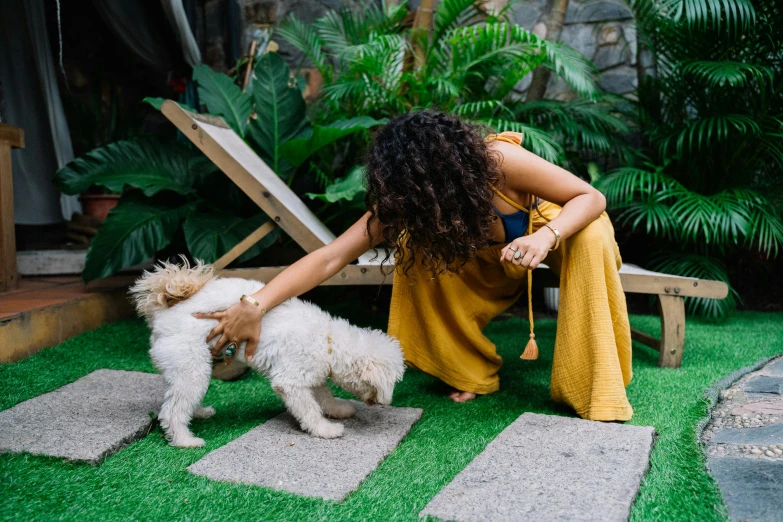 a woman kneeling down petting a small white dog, by Julia Pishtar, pexels contest winner, happening, tropical style, yellow and olive color scheme, backyard, shaggy