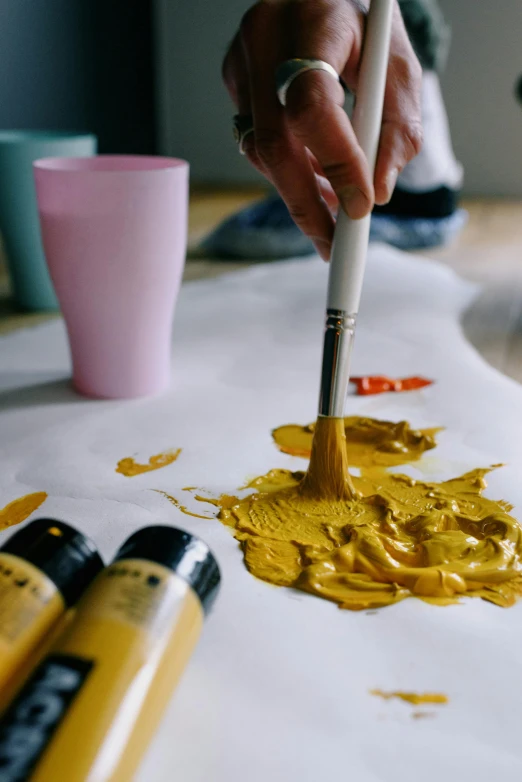 a person is painting on a piece of paper, a hyperrealistic painting, trending on pexels, arbeitsrat für kunst, yellow ochre, paint pour, fashionable, painting of an undercover cup