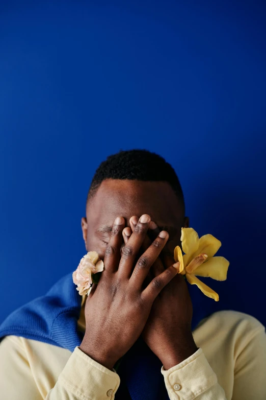 a man holding a flower in front of his face, an album cover, inspired by Paul Georges, trending on unsplash, dark blue skin, mkbhd, hear no evil, yellow and blue