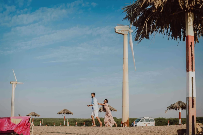 a man and woman standing on top of a sandy beach, turbines, vastayan, summer vibe, people walking around