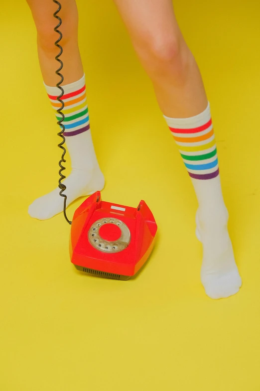 a woman standing next to a red telephone, by Julia Pishtar, antipodeans, striped socks, rainbow accents, studio shot, on a yellow canva