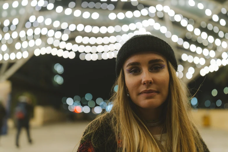 a woman with long blonde hair wearing a beanie, a portrait, inspired by Elsa Bleda, unsplash contest winner, string lights, low quality photo, 50mm photo, slight smirk